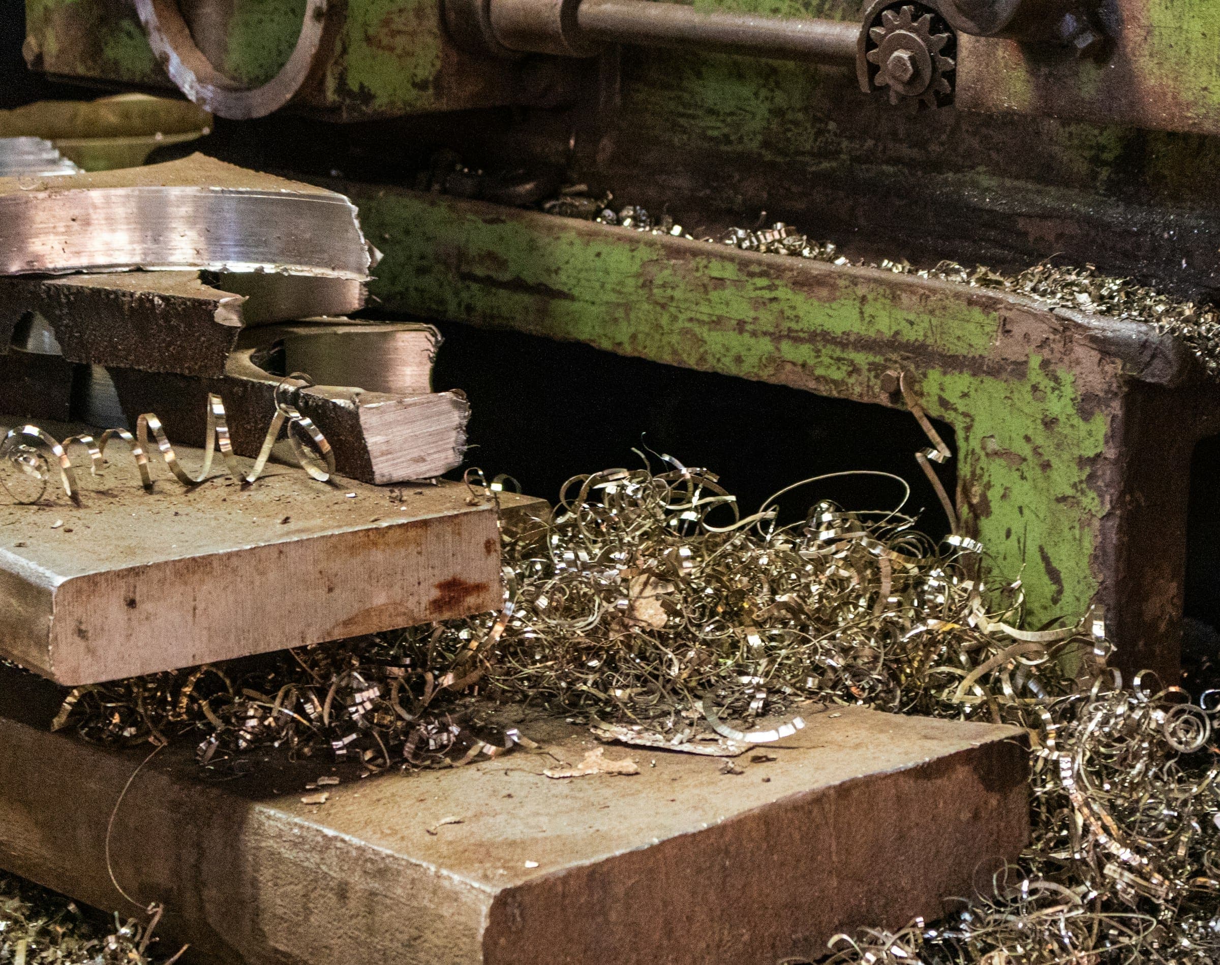Thick steel offcuts on an old machine bed, surrounded by curls of bright metal shavings