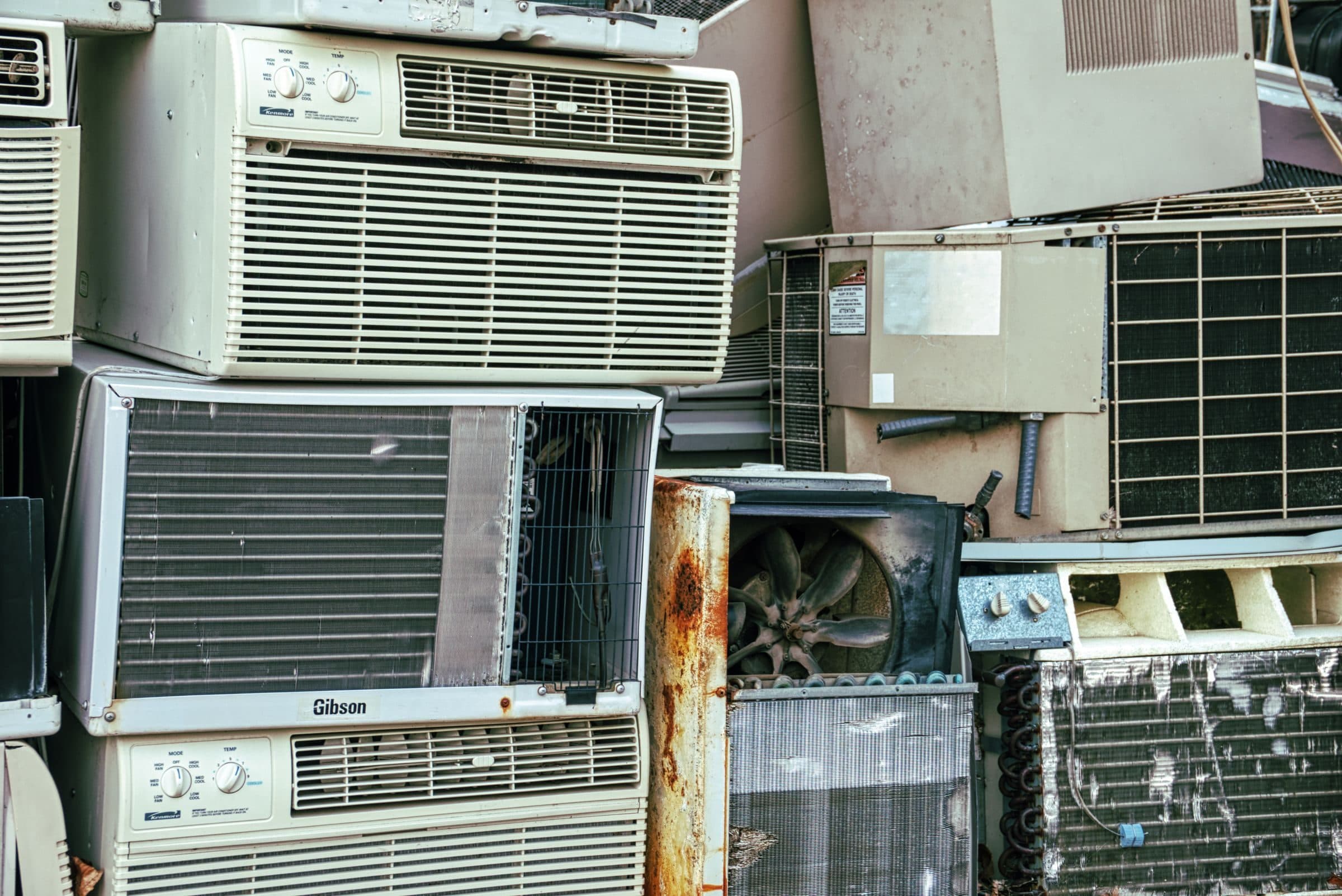 Broken, rusting window air conditioners piled up, one with its fan showing