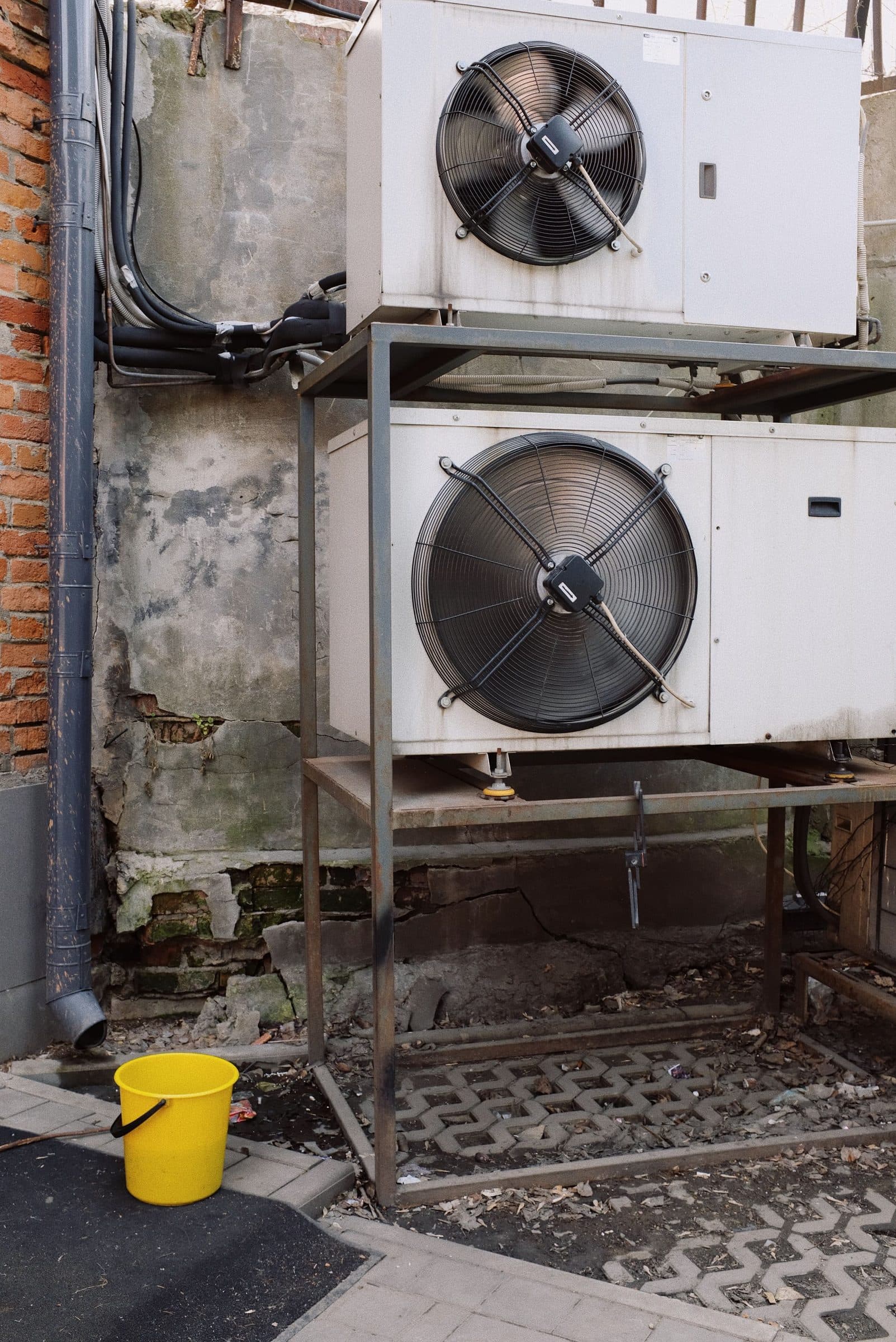 Two refrigeration condensing units with large fans, on a steel frame against a weathered wall