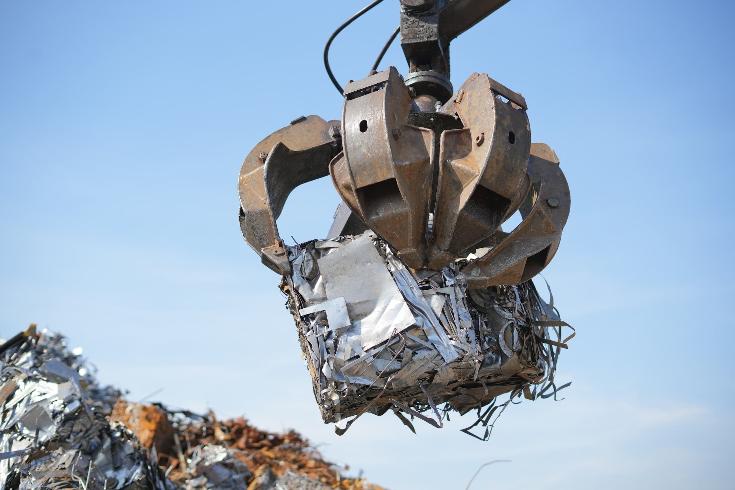 A grapple holding a crushed bale of scrap metal against a blue sky