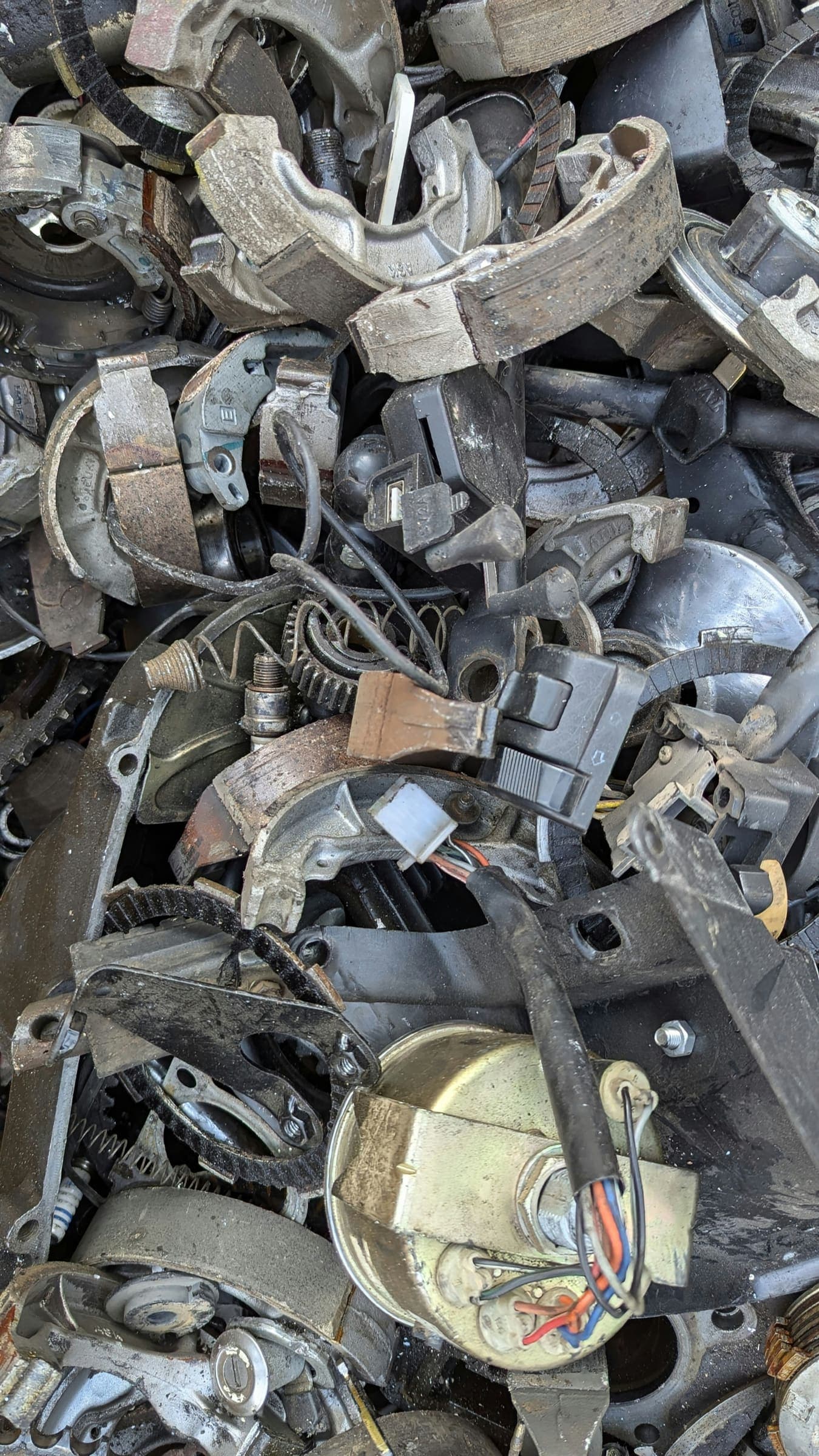 A pile of old motorbike parts, including brake shoes, switches and a speedometer