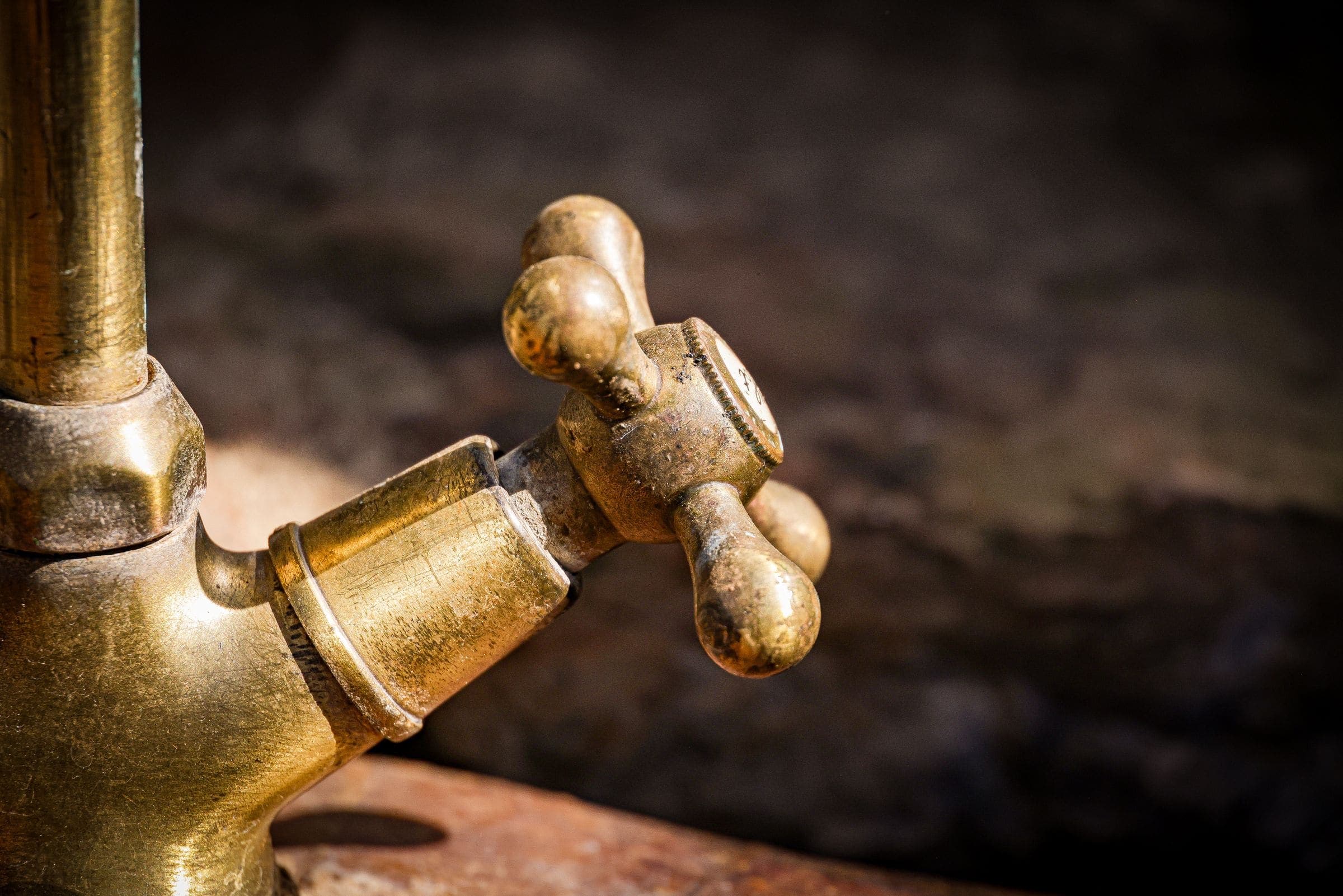 A worn, tarnished brass water tap with a cross-head handle