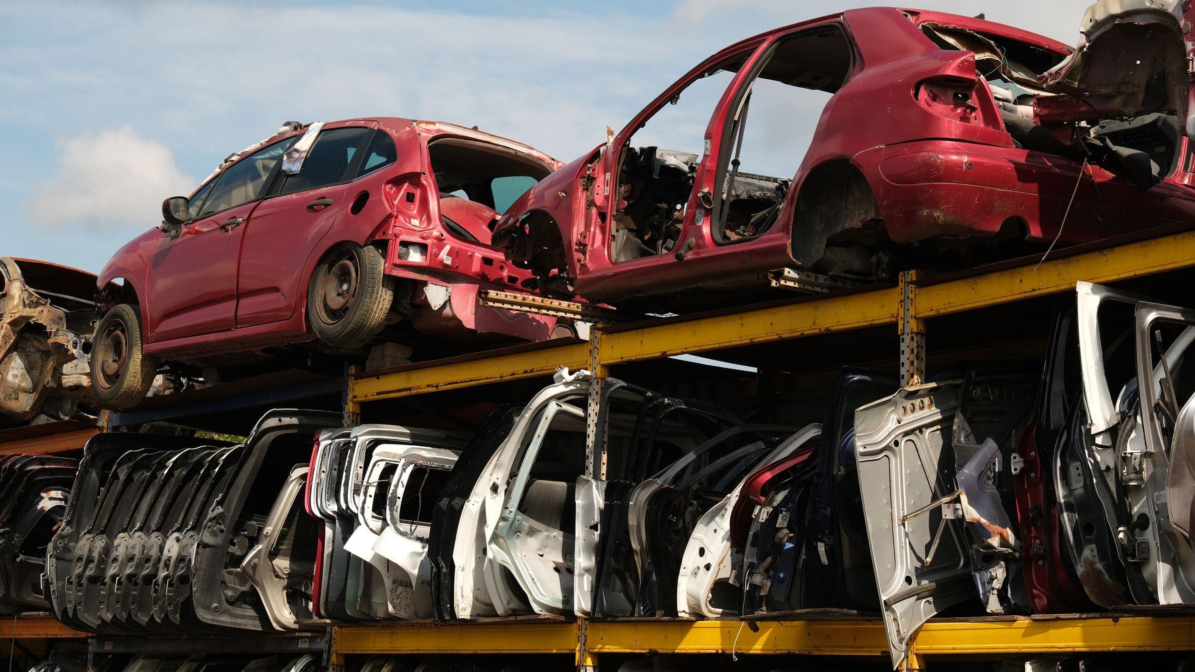 Stripped car bodies stacked on steel racks above rows of car doors in a wrecking yard