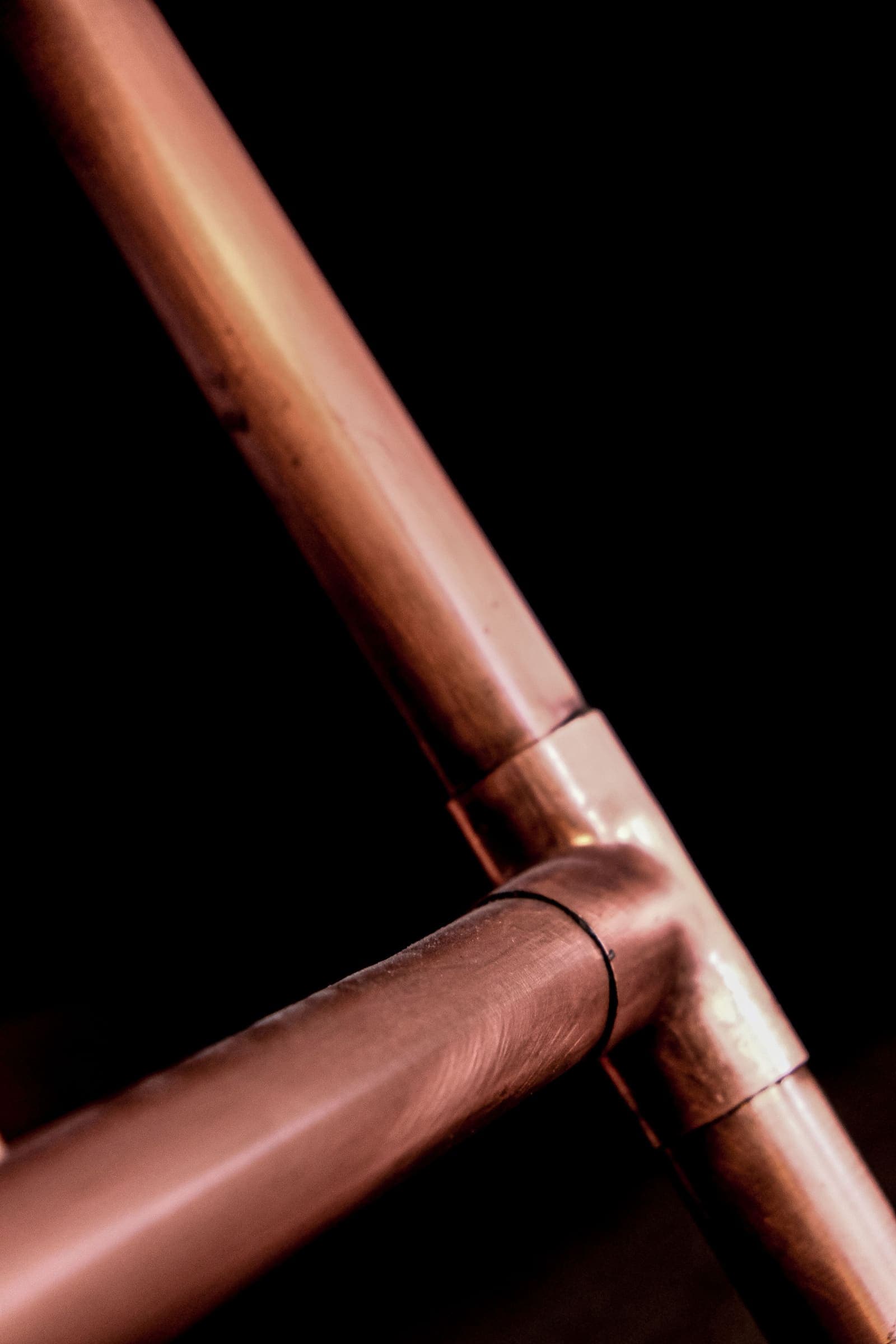 Copper pipes joined with a tee fitting against a black background