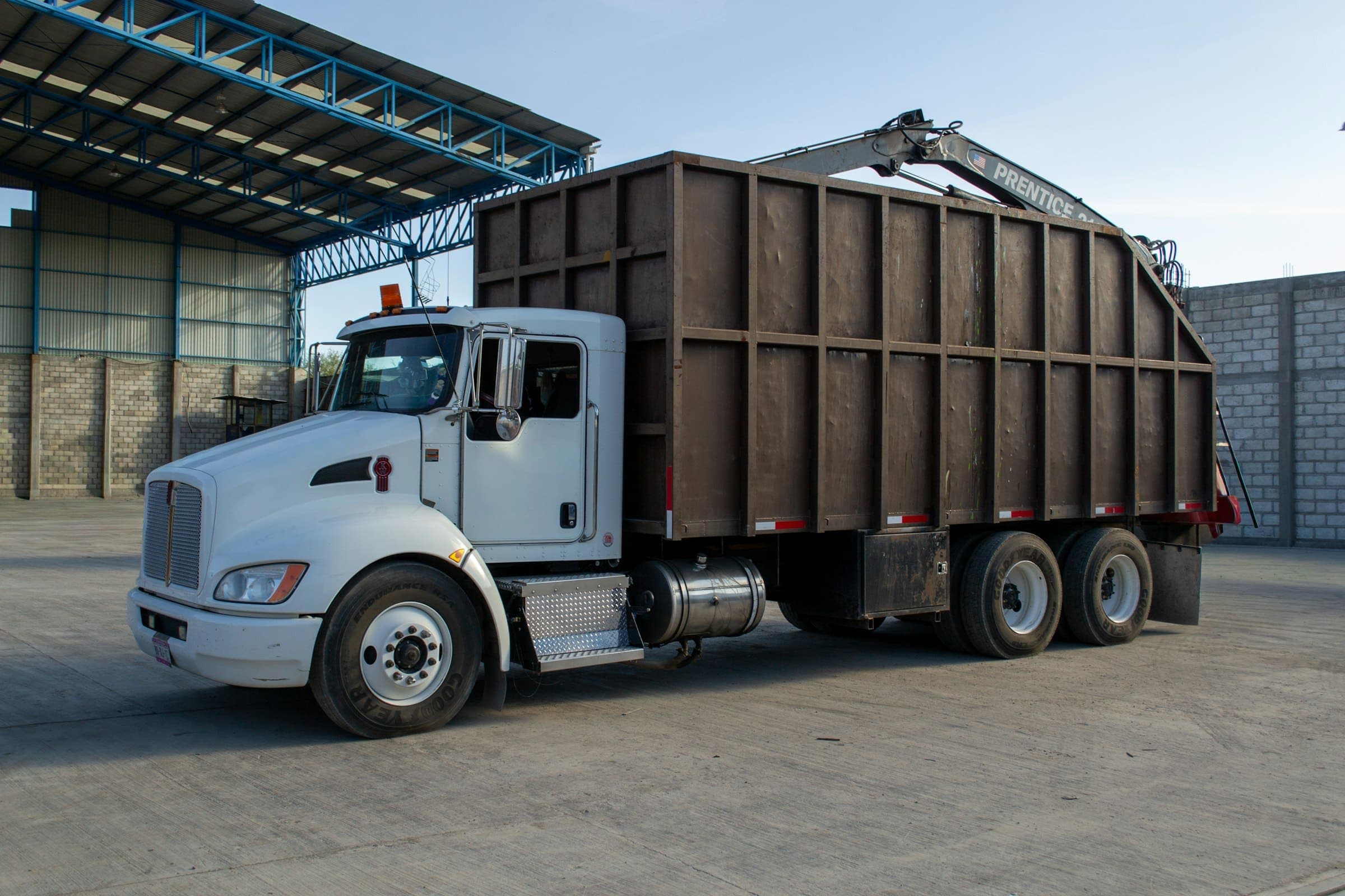 Grapple truck for collections A white truck with a tall steel body and a folded grapple crane parked in a concrete yard