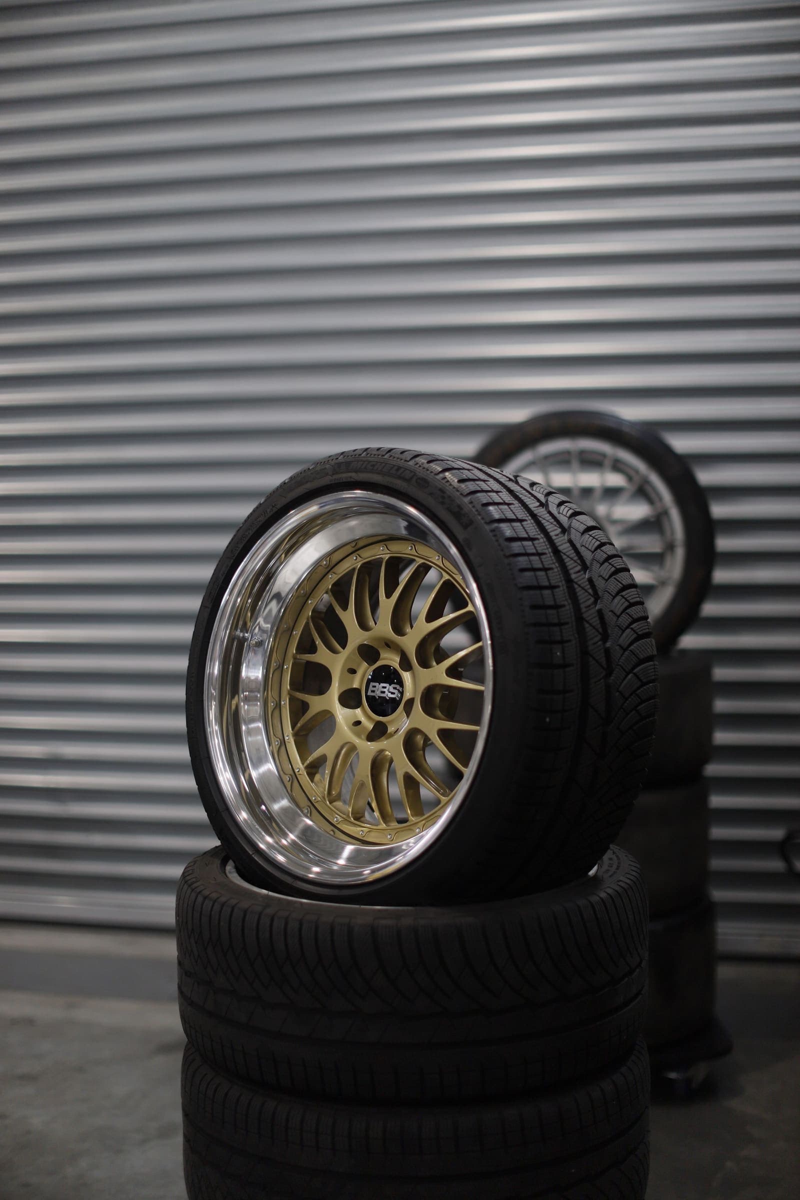 Gold mesh alloy wheel A gold mesh-style alloy wheel on a stack of tyres in front of a roller door