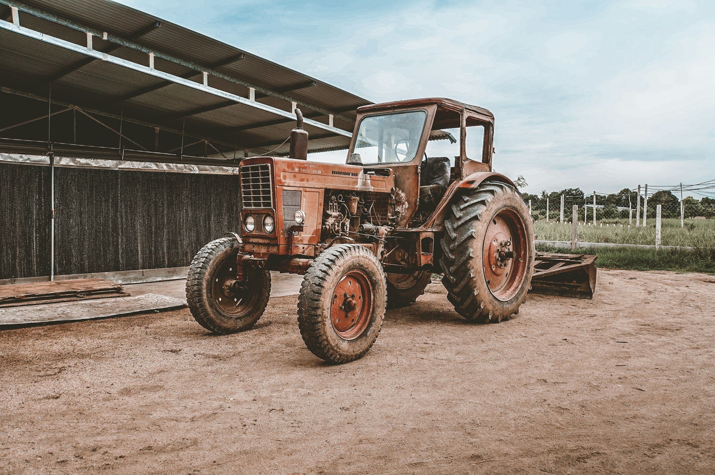 Rusty old tractor A weathered, rusty farm tractor parked beside an open-sided shed